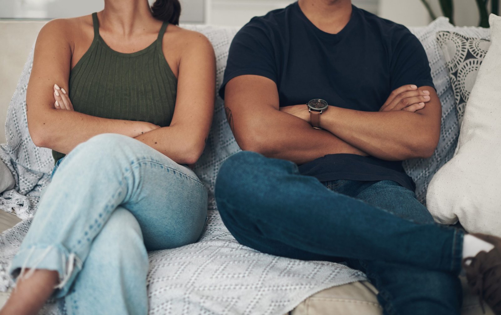 Couple sitting on opposite ends of a couch with arms crossed, facing away from each other – representing tension in a relationship. Link to Divorce services.